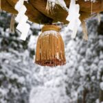 雪に覆われた雄山神社の注連縄の房。背景には雪景色の森が広がっている。