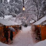 雪が降りしきる冬の朝、雄山神社の参道に並ぶ屋台。橙色の灯りが薄暗い雪景色を照らしている。