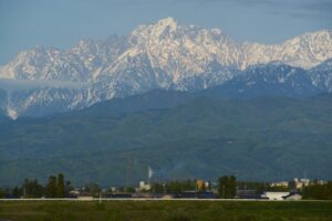 緑の濃い里山の奥に、残雪を抱いた剱岳がそびえる風景
