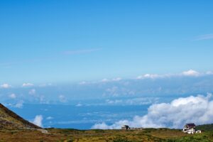 立山の高原から雲海越しに富山平野を見下ろす景色。手前には山小屋と高原の草地が広がっている。