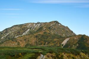 青空を背景に、紅葉と緑がまだらに広がる奥大日岳の山肌