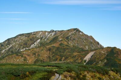 青空を背景に、紅葉と緑がまだらに広がる奥大日岳の山肌