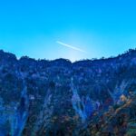 称名滝上空の青空を飛行機雲が横切る、紅葉に包まれた山並み