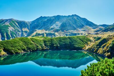 立山の雄山が青空を背景にそびえ、手前のみくりが池に山並みと紅葉が鮮明に映り込んでいる