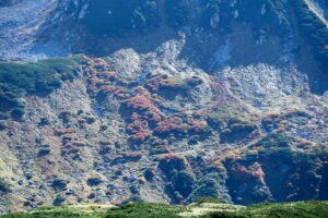 雄山の中腹の岩場に点在するナナカマドなどの紅葉が赤や橙に色づいている様子