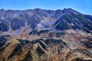 雄山の険しい岩稜の下に、赤や黄に色づいた紅葉が斜面に広がる立山の秋景色