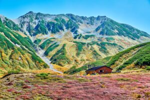雷鳥沢の山小屋を前景に、赤や黄色に色づいた草紅葉と、背後にそびえる雄大な立山の山並み