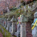 富山市五百羅漢の参道に並ぶ石仏と石灯籠。色とりどりの布がかけられた石仏と落ち葉が、秋の深まりを感じさせる。