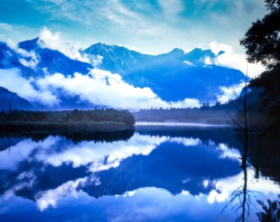 上高地の大正池から望む穂高連峰。雲と山が湖面に映り込む風景写真。