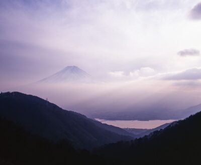 霧と柔らかな光に包まれた富士山と、その麓に広がる河口湖を望む風景写真。