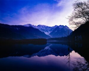 上高地の大正池から望む穂高連峰。初冠雪の山並みが湖面に映る風景写真。