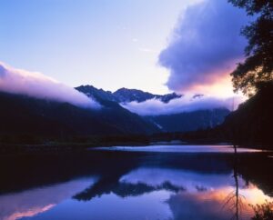 上高地の大正池に穂高連峰が映り込み、夕暮れの光と雲が山を包む幻想的な風景