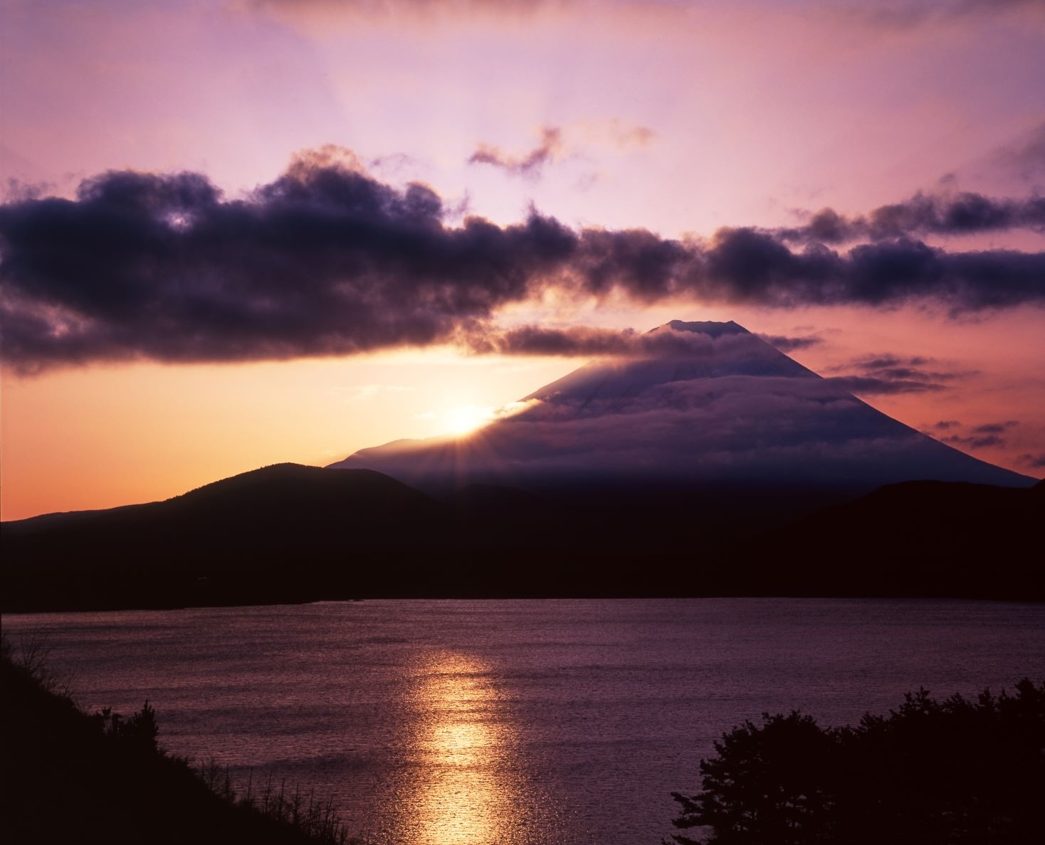 夜明けの本栖湖の湖面に、雲に包まれた富士山と昇る朝日が映える風景写真。