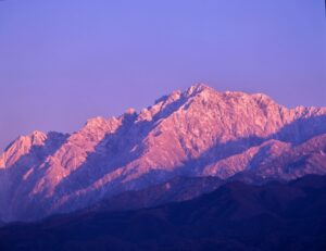 夕暮れの斜光を受け、雪をまとった剱岳が赤紫色に染まる遠景
