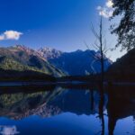 秋の大正池から望む穂高連峰。紅葉した岩肌と山影が湖面に映る風景写真。