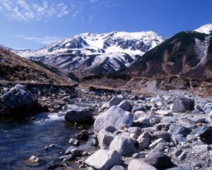 雷鳥沢の清流と岩場の奥に、雪をまとった立山連峰が広がる初冬の景色