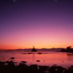 夜明け前の雨晴海岸の風景。紫から朱色に染まる空と海、岩のシルエットが印象的な写真。