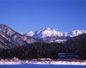 冬の里山と集落の奥に、雪に覆われた剱岳が青空に映える風景